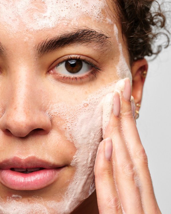 A person massaging the Skinfix Balancing Soft-Foam Clay Cleanser into their face, with a rich foam lather visible across the skin.