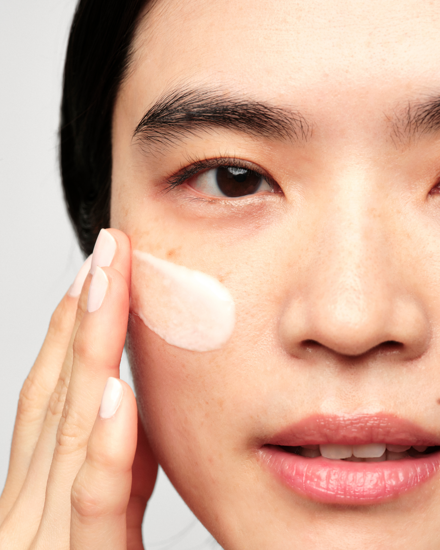 Close-up of a person applying or spreading a serum onto their cheek with their other hand, showing a smooth, glossy texture on the skin.
