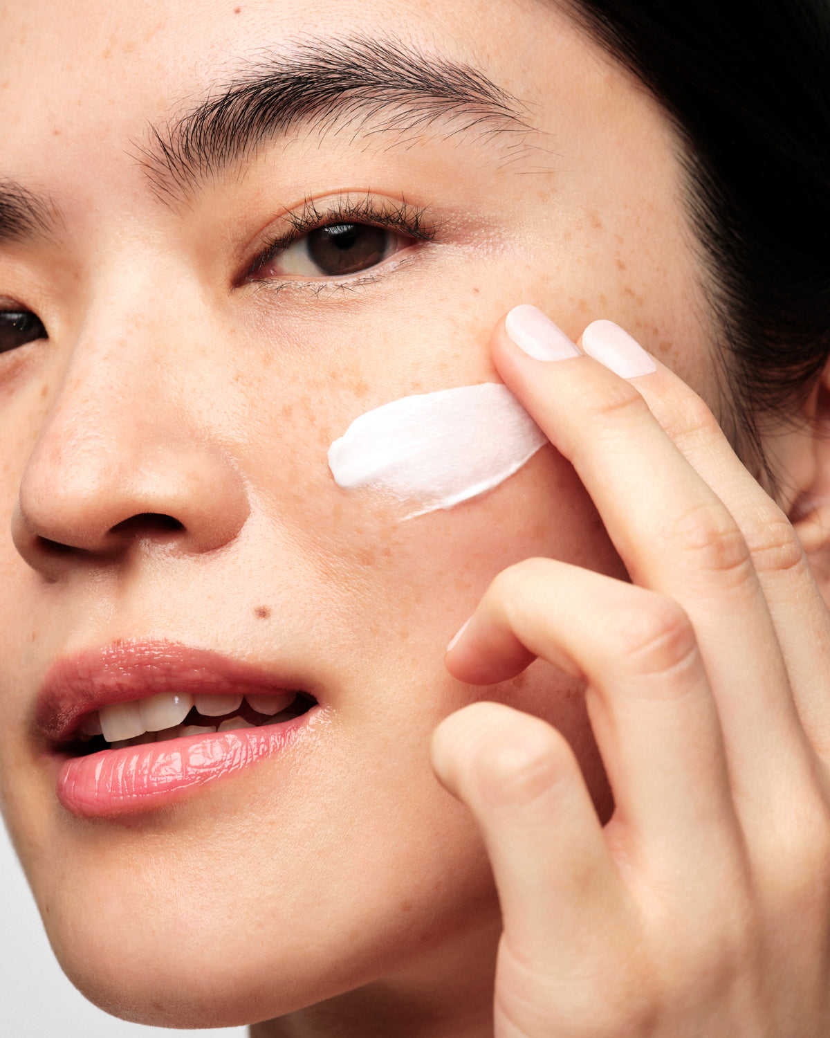 Woman applying white cream to cheek with fingertip.