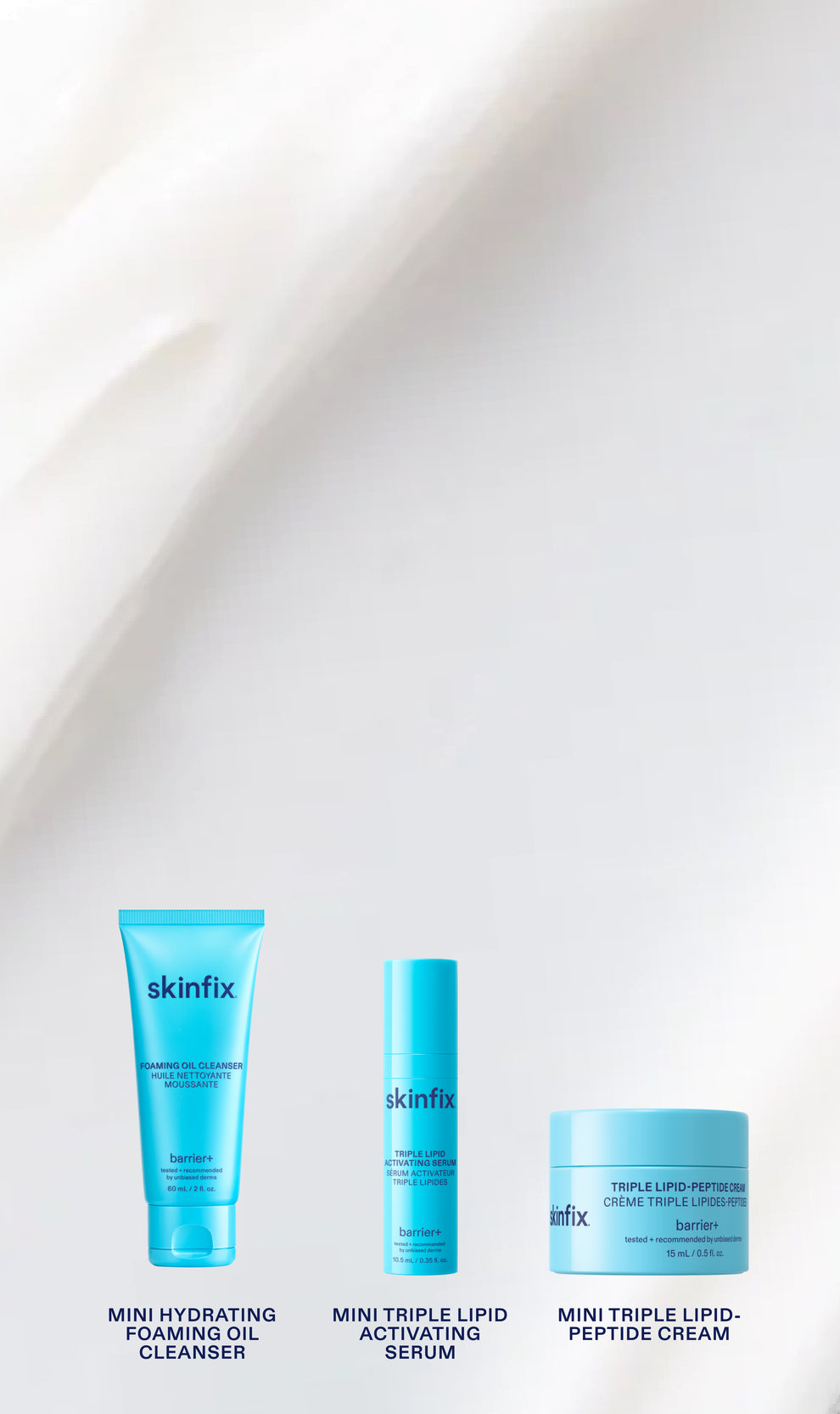 Three skincare products from skinfix lined up on a white background with soft draped fabric. The products are: Mini Hydrating Foaming Oil Cleanser in a bright blue squeeze tube, Mini Triple Lipid Activating Serum in a matching blue cylindrical bottle, and Mini Triple Lipid-Peptide Cream in a light blue cream jar.