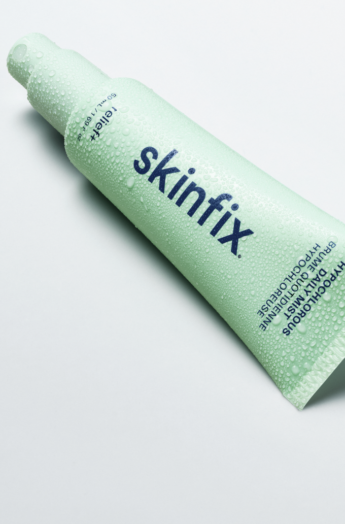 A light green tube Skinfix Hypochlorous Dailt Mist layong on white background, covered in water droplets.