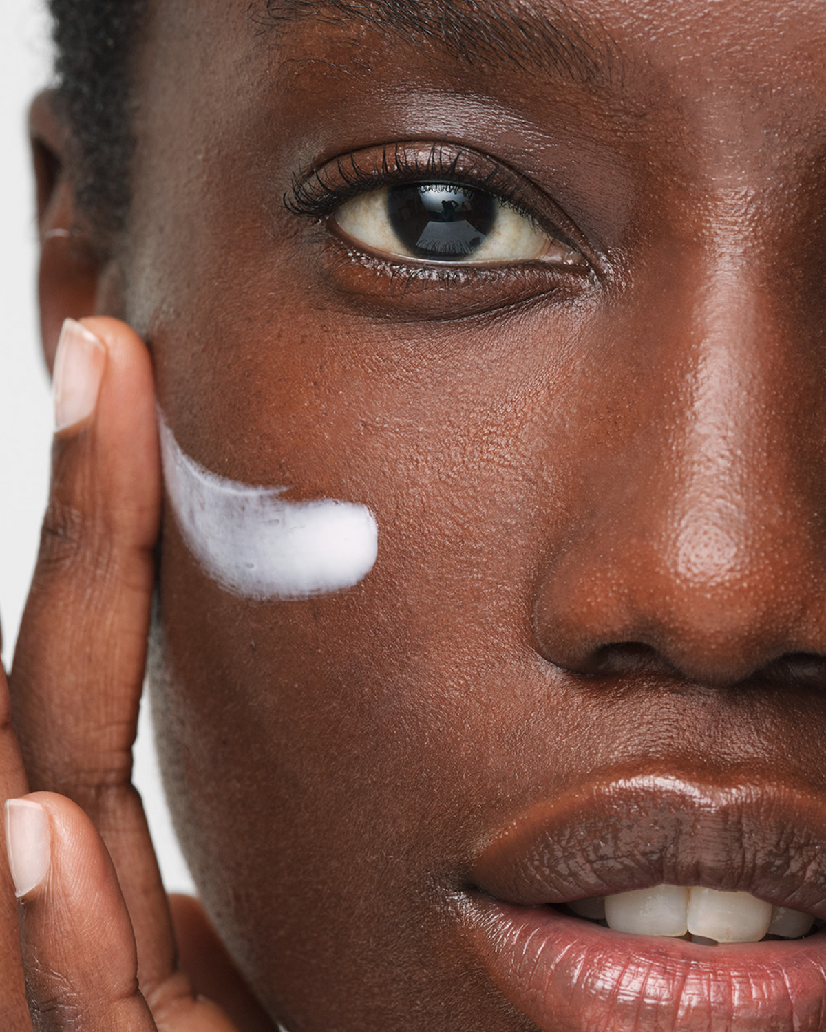 Woman looking into camera applying Triple Lipid-Peptide Cream to cheek with fingertips.