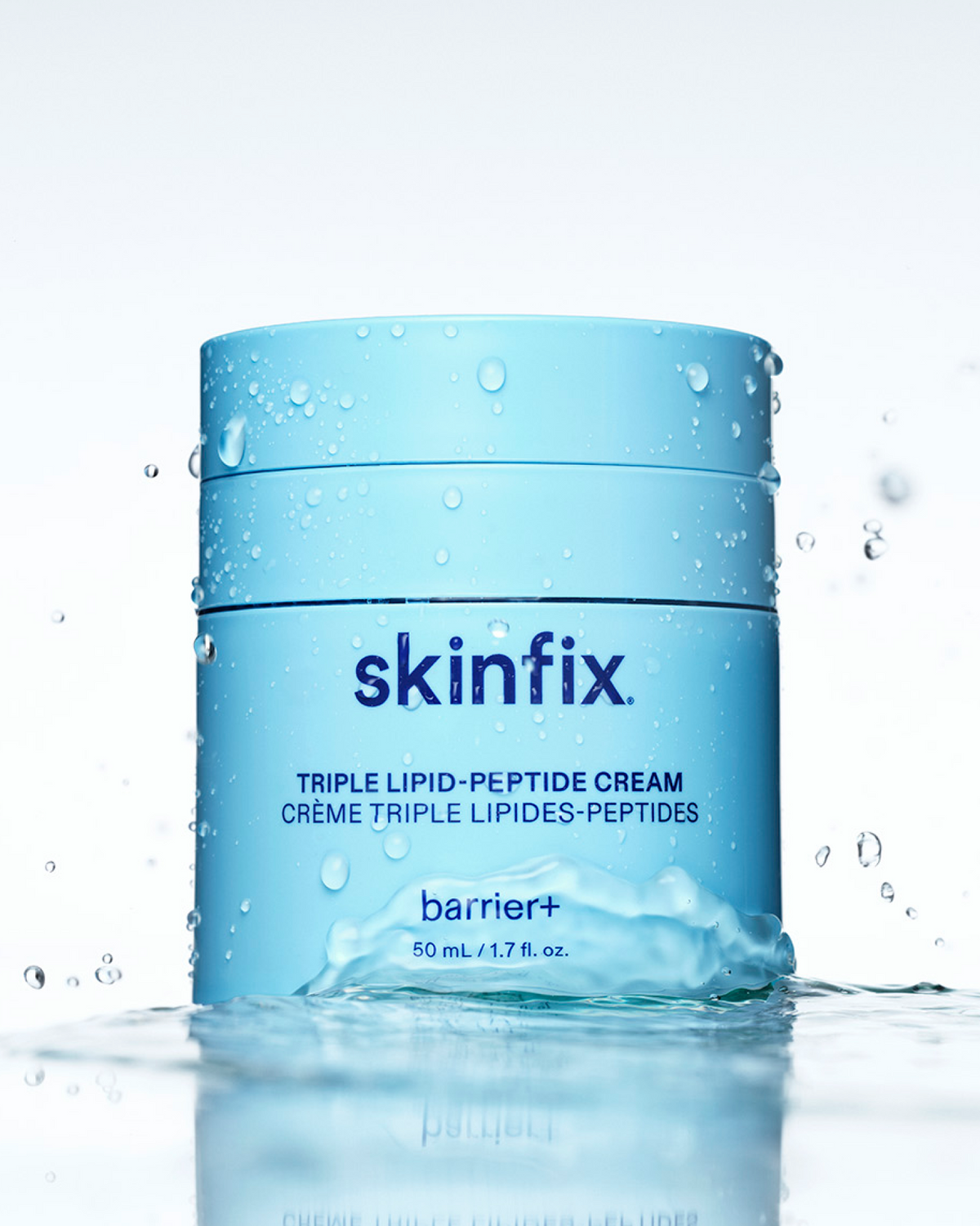 A light blue jar of skinfix Barrier+ Triple Lipid-Peptide Cream, covered in water droplets and partially submerged in water with a splash, on a white background.