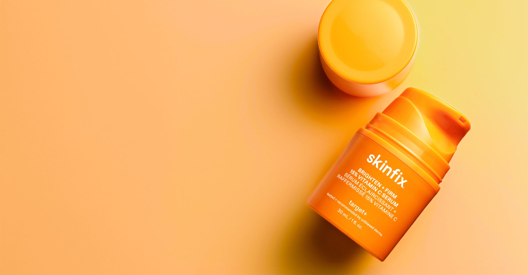 Skinfix Brighten + Firm 15% Vitamin C Serum, with the lid removed, on an orange gradient background.