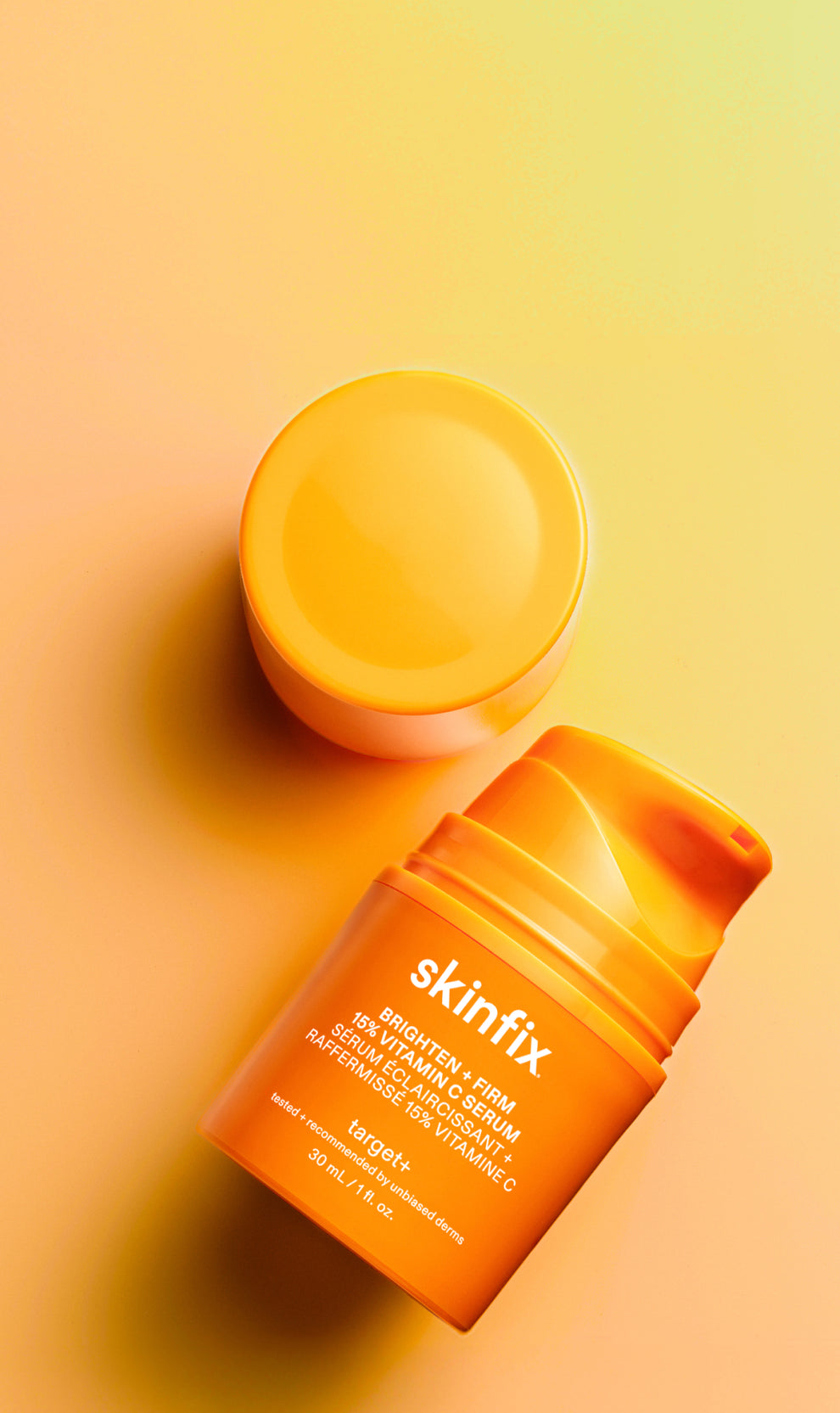 Skinfix Brighten + Firm 15% Vitamin C Serum, with the lid removed, on an orange gradient background.